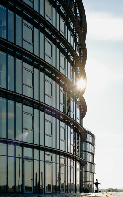 Moderne Glasfassade eines Bürogebäudes bei Sonnenuntergang, mit reflektierendem Licht und geschwungener Architektur